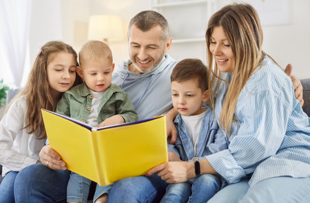 Big family of five, caring happy mother, father, three children reading book story at home with little kids sitting on sofa, family spending leisure time together, loving parents having fun togetherの写真素材