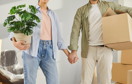 Moving day, young family entering new flat, celebrating relocation to own home, holding pot flower,...