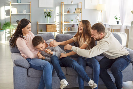 Joyful funny family at home, parents and children adult happy excited tickling boy son in joy,...