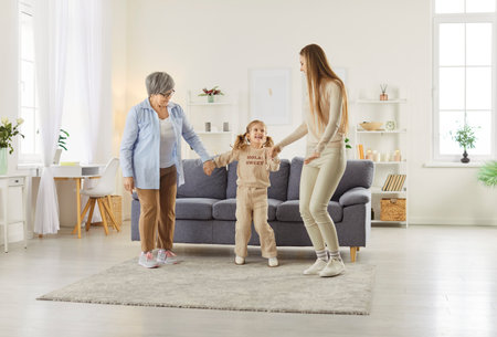 Happy smiling senior grandmother, mother and little child girl having fun dancing in the living room...