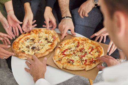Top view close up hands of a young people friends gathering in pizzeria or at home together eating tasty Italian food taking pizza slices enjoying party indoors. Food delivery concept.の写真素材