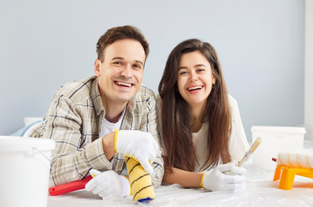 Joyful positive young couple, happy husband and wife enjoying, planning interior decoration work, artwork on wall, painting together, smiling laughing, having repair in new apartment, home improvementの写真素材