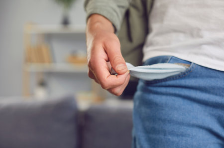 Close-up of a young poor man in casual clothes turning inside and showing empty pocket with no money standing in living room at home. Moneyless, bankrupt, financial crisis and poverty conceptの写真素材