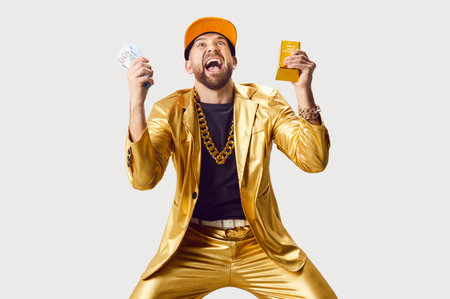 Happy excited shocked funny young man in golden suit and cap holding money dollars cash banknotes and gold bar in hands isolated on white studio background. Finance, success and investment concept.の写真素材