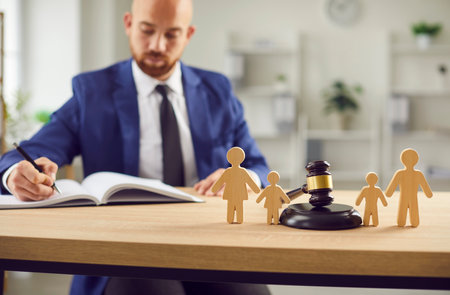 Judge gavel stands with family wooden figures, attorney working with documents in court on background. Judgement in family matters like custody, divorce, and children, pursuit of justice.の写真素材