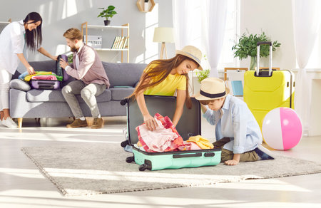 Family preparing for summer vacation or travel, with the children packing suitcases at home. Excitement of the upcoming trip, showcasing the joy of holiday preparation and family bonding.の写真素材