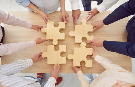 Top view of people hands assembling big wooden puzzle standing in circle in office. Coworkers join jigsaw pieces finding solution, working on project together. Support and teamwork concept.の写真素材