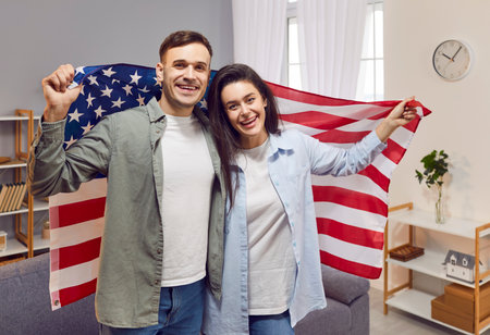 Heartwarming portrait of a happy family wrapped in an American flag, celebrating Independence Day. Their patriotic spirit shines through as proud citizens of the USA, enjoying the festivities at home.の写真素材