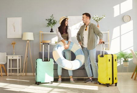 Full length of happy young couple tourists man and woman standing in living room at home with packed suitcases ready for holiday trip. Vacation, travelling and summer journey concept.の写真素材
