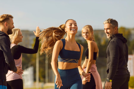 Portrait of young athletic girl running to the finish to friends supporting her standing in city...