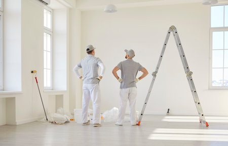 Professional wall painters working in newly constructed house or apartment building. Two men with painting equipment standing in spacious interior and looking at white wall. Home renovation conceptの写真素材