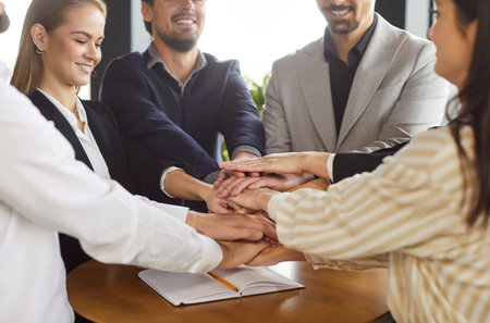 Group of business people or coworkers standing together in a circle in an office, holding hands. Teamwork, collaboration, and shared achievement as they unite for professional goals and success.の写真素材