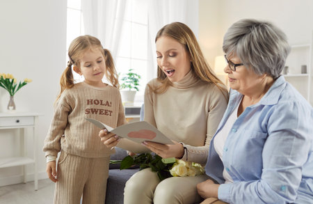 Three female generations family fun at home card getting with heart love, cute little granddaughter girl, mother, grandmother, beloved granny, funny grandchild, young mom enjoy leisure time togetherの写真素材