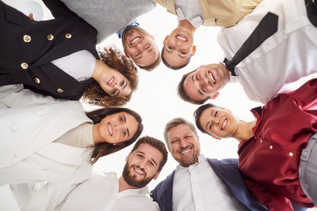Bottom view portrait of a joyful smiling business people looking down into camera. Happy company employees men and women standing in a circle in office and smiling. Teamwork concept.の写真素材