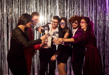Group of happy friends enjoys an evening party at a nightclub, drinking champagne from glasses and...
