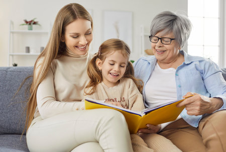 Three female generations family fun at home reading book story, cute little granddaughter girl,...