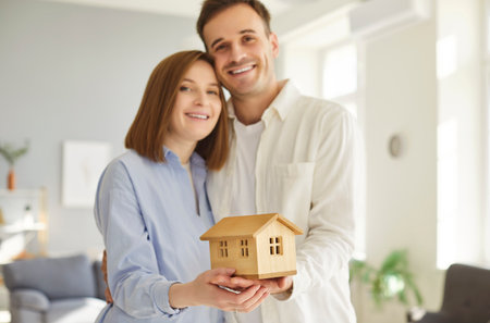Smiling and happy family couple celebrating the purchase of new real estate at home. They hold a symbolic figurine, reflecting happiness, togetherness, and shared joy of ownership.の写真素材