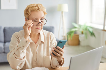 Serious focused woman, pensive lady using mobile phone for work at desk, communication, thinking on problems, reading online chat message, cellphone call, social media network, looking in glassesの写真素材
