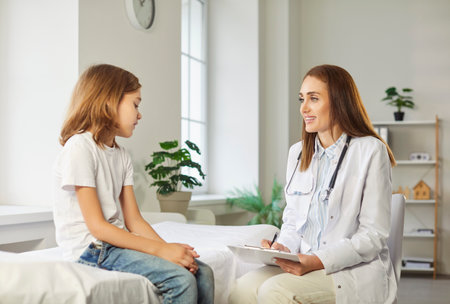 Friendly female child doctor pediatrician giving consultation and talking with little boy patient sitting on couch in medical clinic in exam room during checkup. Pediatrics and medicine conceptの写真素材