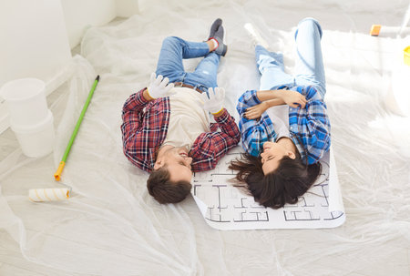 Happy and friendly husband and wife lie on the floor, dreaming and planning future together during the renovation of new home or apartment. Family connection and construction aspirations.の写真素材