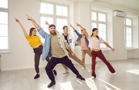 Group of energetic hip hop dancers have fun rehearsing dance moves while learning new dance. Talented young people in casual clothes dance together in bright and spacious dance studio.の写真素材