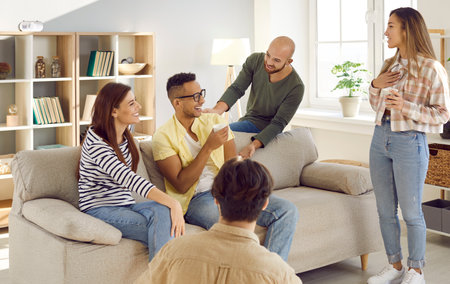 Diverse group of happy young friends having fun at cozy party at home. Cheerful mixed race multi ethnic people talking, drinking coffee, telling funny stories, laughing and enjoying good time togetherの写真素材