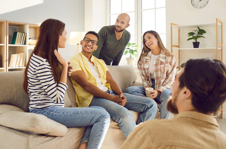 Spending great time with best friends. Group of young multiracial people have fun communicating with each other during meeting at home. Men and women tell their stories sitting on sofa in living room.の写真素材