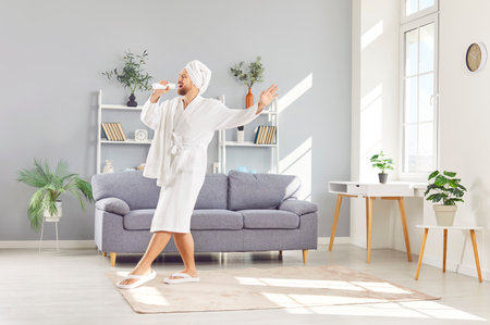 Happy man in a bathrobe dancing and singing to music at home after a morning shower. Joyful morning routine, showcasing the uplifting energy of starting the day with dancing, singing, and music.の写真素材