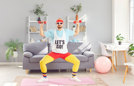 Bald man in a funny outfit and sunglasses performs dumbbell exercises and squats at home gym. His fitness training and workout routine show a blend of humor and dedication to sport.の写真素材