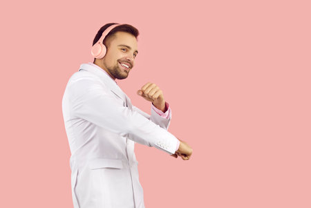 Overjoyed young man in suit isolated on pink studio background wear wireless headphones listen to music. Smiling guy in earphones enjoy good quality sound in modern device. Technology.の写真素材