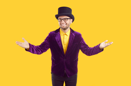 Male entertainer welcoming you to theatrical performance, holiday festival or circus show. Man in purple velvet suit and top hat standing isolated on yellow background, spreading his arms and smilingの写真素材