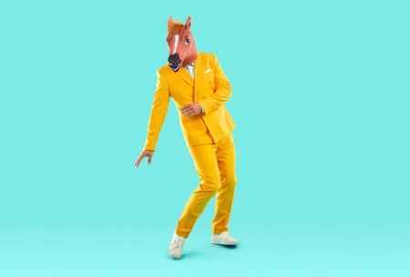 Full length portrait of horse young man dancing. Funny man wearing horse latex head mask and stylish elegant yellow suit standing over isolated studio backgroundの写真素材