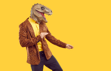Funny reptile dancing on yellow studio background. Side view of happy man in leopard jacket and dinosaur mask dancing isolated on yellow copy space background. Halloween party conceptの写真素材