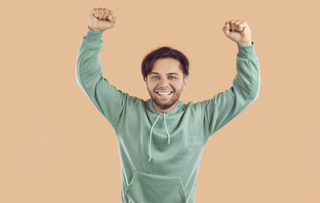 Portrait of cheerful young man celebrating victory with raised fists. Handsome satisfied man celebrating success, expressing positive emotions over isolated studio backgroundの写真素材