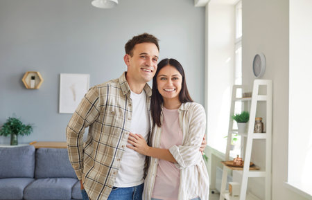 Portrait of a young cheerful smiling man and woman in casual clothes hugging indoors standing in the living room at home. Happy couple in love. Relationships, romance and Valentines day concept.の写真素材