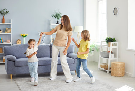 Full length portrait of young happy family of mother and two kids having fun and dancing in the living room at home. Woman enjoying spending time with children. Family leisure and mothers day conceptの写真素材