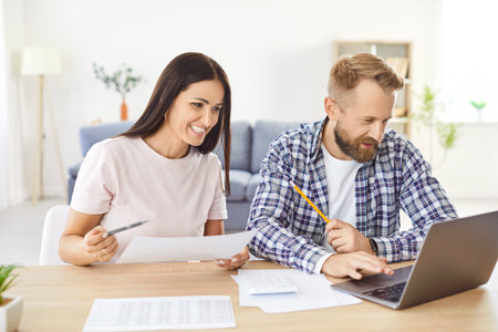 Family couple working together at home on a laptop, managing money or invoices, paying bills, and handling debts or investments. Teamwork in financial planning and money management in a household.の写真素材