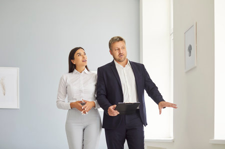 Expert realtor presenting to young woman bright spacious real estate, telling about progress of construction works or future design. Female client exploring options of house for purchase or rent.の写真素材