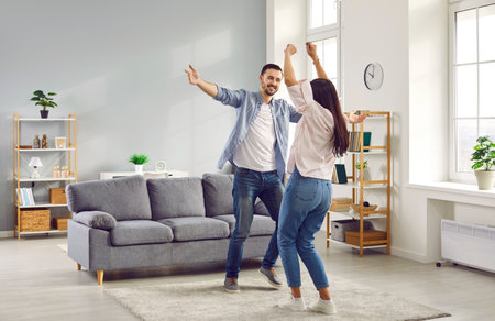 Happy family couple having fun together and dancing in the living room at home. Young man and woman celebrating something joyful like buying a new apartment or paying off mortgage earlyの写真素材