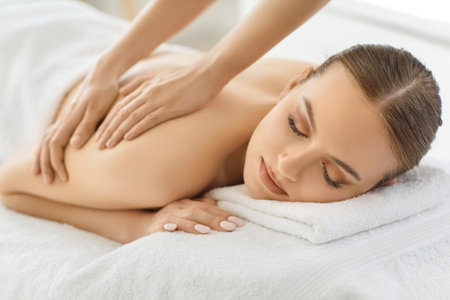 Indoor shot of relaxed woman enjoying spa treatment in salon, getting massage for back, has body care treatment, lying on white towel. Setting evoking sense of serenity and wellbeingの写真素材
