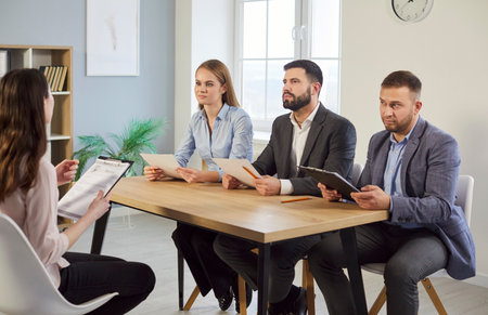Diverse HR managers talking with job employee, impression of candidate, employers listen to applicant at interview of candidature, recruitment, sitting at conference table discussing job experienceの写真素材
