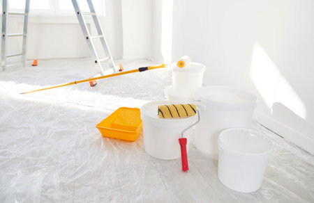 Close up of buckets with paint rollers standing in empty new house with freshly painted white walls with step ladder in background. Renovation process in apartment. Home repair and moving day conceptの写真素材