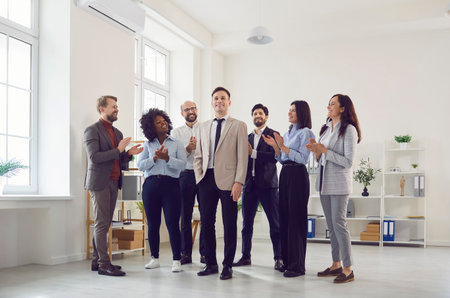 Successful Caucasian businessman stands surrounded by applauding coworkers in the office. The team is celebrating success, demonstrating collaboration, teamwork, and mutual support.の写真素材