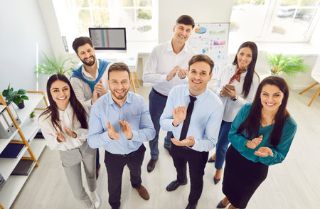 Top view of a group of happy smiling business people men and women looking at camera, smiling and applauding. Company employees or a group of staff standing in the office cheerfully.の写真素材