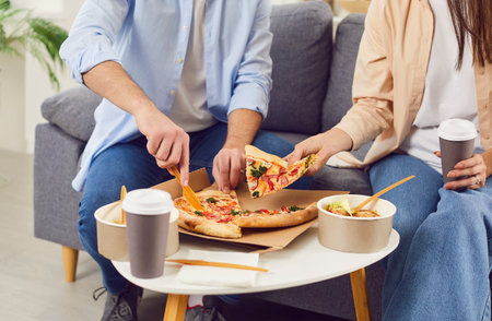 Close up shot of a family couple eating a meal of takeaway pizza at home. Cozy moment of togetherness, highlighting the convenience and comfort of food delivery for a relaxed lunch.の写真素材
