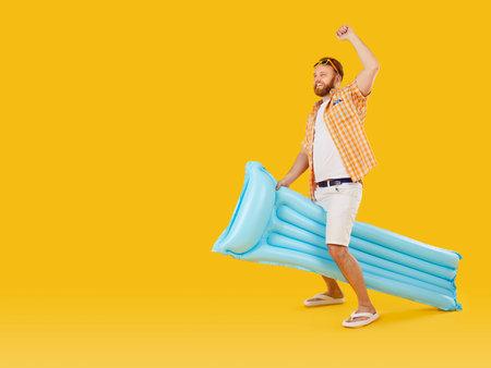 Man joyfully celebrates summer vacation or holiday, with an inflatable mattress, symbolizing travel and beach fun, on orange background, expressing happiness and the excitement of the journey.の写真素材