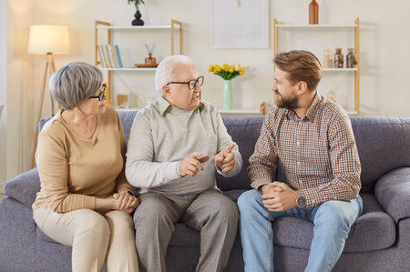 Portrait of happy joyful smiling family of senior mother, father and their adult son sitting on sofa in living room at home and talking together. Man visiting his old parents. Family leisure concept.の写真素材