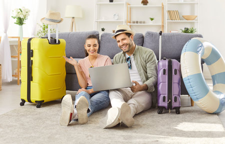 Tourist couple planning summer trip online from home with laptop happy packing luggage bag for traveling, vacation trip, big suitcase for honeymoon, dreaming, wearing summer trip holiday beach wearの写真素材