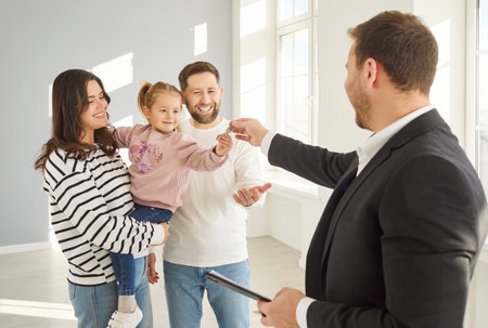 Happy young family couple with small child girl moving new house, male real estate agent giving...