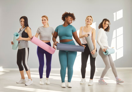 Sporty diverse women pose in full length with fitness mats prrepare for fitness training lead active healthy lifestyle smile happily. Woman and her friends rest from physical activity recover strengthの写真素材
